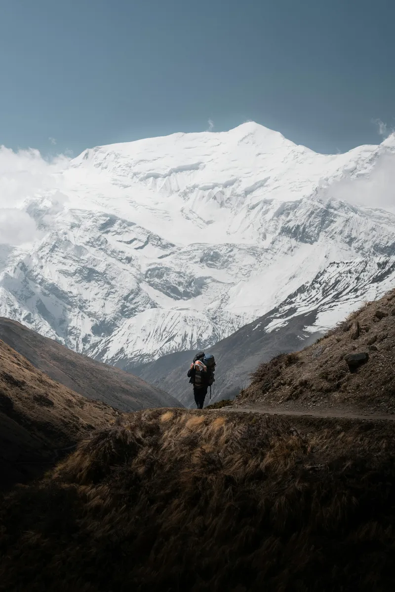 A lone mountain porter walking beneath the vast Annapurna massif